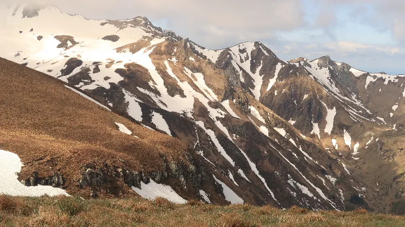 photo of a mountain landscape with patched of yellow grass poking up through the leftover of winter snow
